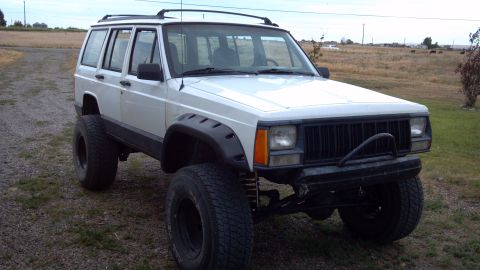 1995 Jeep Cherokee - A white 1995 Jeep Cherokee is parked outdoors, modified with a lifted suspension and large tires.