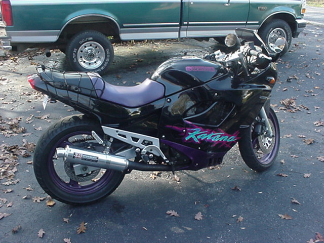 Black sportbike motorcycle with purple seat and 'Katana' graphics parked near a green pickup truck