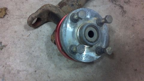 1995 Jeep Cherokee - Wheel hub assembly part with a rusty metal arm and red spacer on a concrete surface.