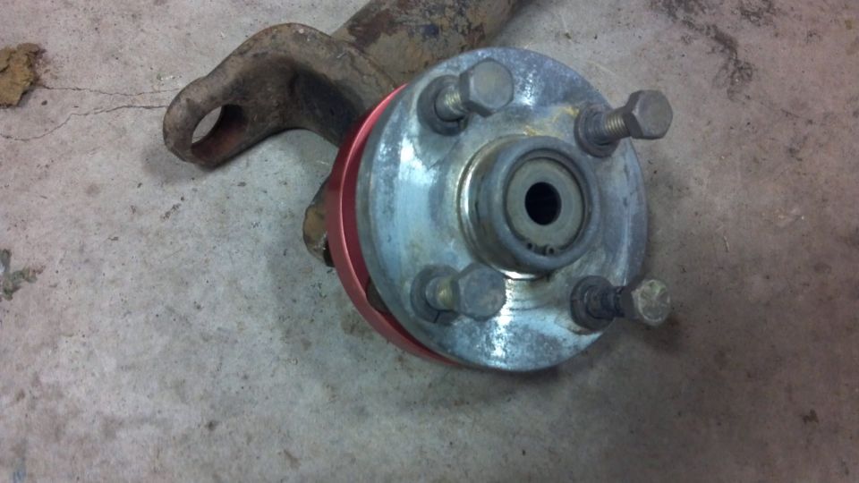 Close-up of a rusty metal arm attached to a wheel hub assembly with a red spacer