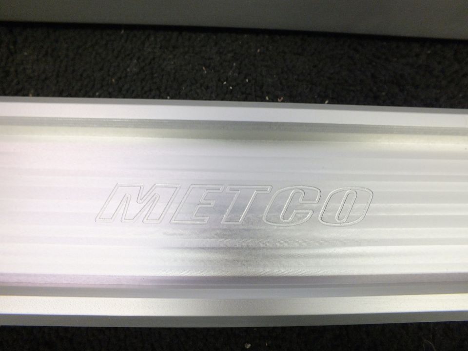 Billet aluminum suspension arm engraved with METCO logo on dark carpet