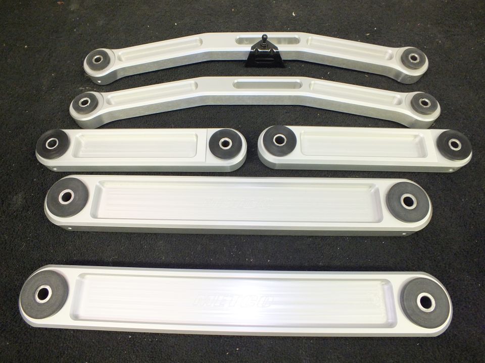 Set of billet aluminum suspension control arms laid out on dark carpet