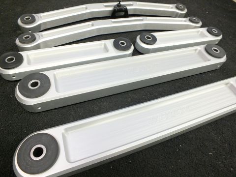 2003 Ford Crown Victoria - Machined aluminum control arms with pressed bushings spread across dark carpet.