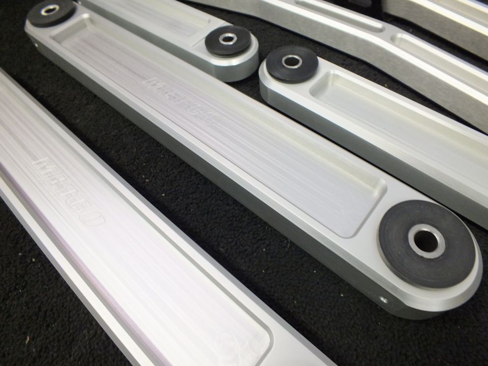 Set of billet aluminum control arms with rubber bushings arranged on dark padded surface