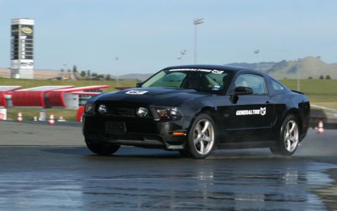 2007 Ford Mustang - A black Ford Mustang with 'General Tire' decals drives on a wet racetrack.
