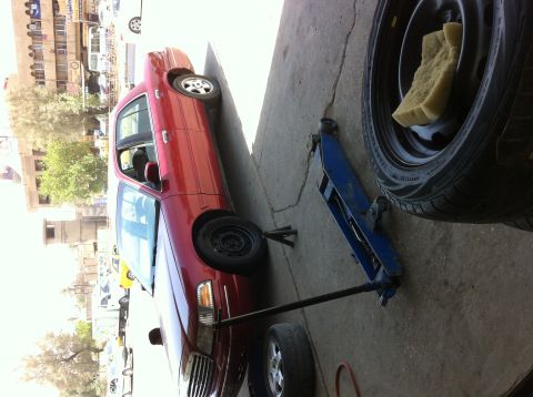 1998 Ford Crown Victoria - A red 1998 Ford Crown Victoria is shown on a jack, with a spare tire and jack equipment visible.