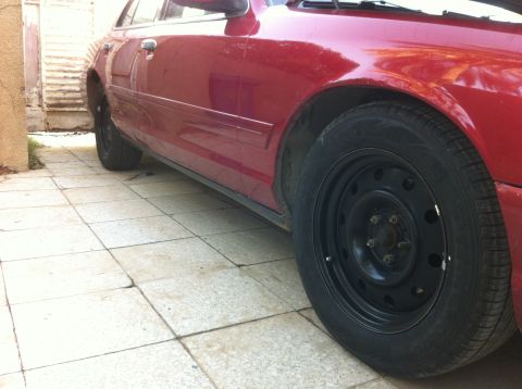 1998 Ford Crown Victoria - The side profile of a red sedan with black steel wheels is shown parked on a tiled surface.