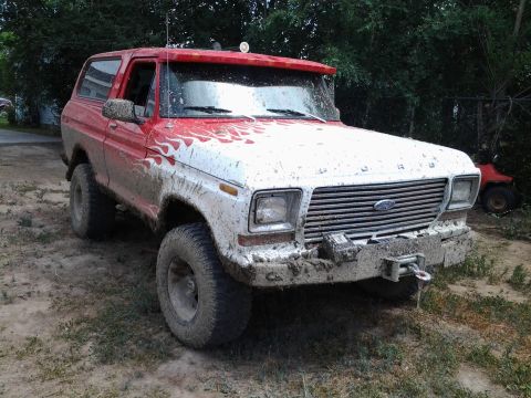 1979 Ford Bronco - This mud-splattered 1979 Ford Bronco features red and white paint with flame decals, ready for off-road adventure.