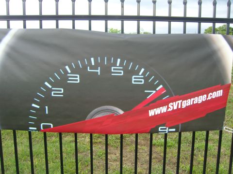 2007 Ford Mustang - A banner displaying a car's tachometer and a website address is hung on a fence.