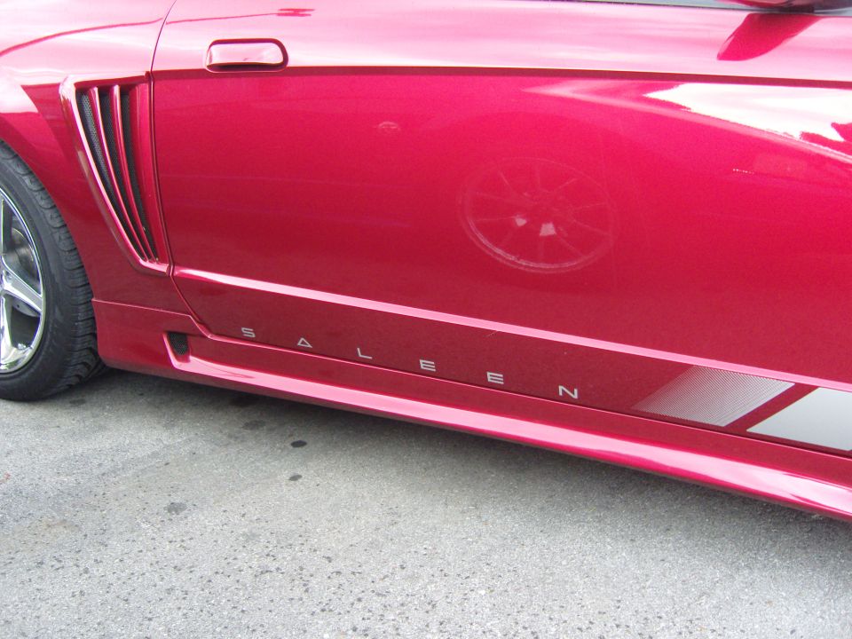 Red Saleen Mustang with 'SALEEN' text on the rocker panel. Shows side vent and part of the wheel