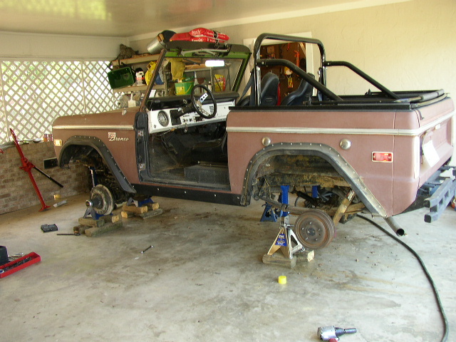 Old Ford Bronco on jack stands, doors off, undergoing restoration in a garage