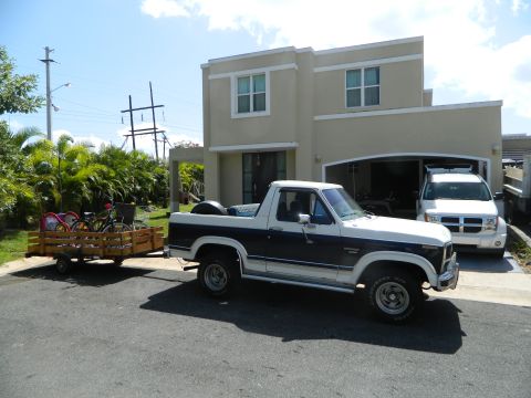 1984 Ford Bronco - A two-tone Ford Bronco tows a trailer with bicycles in front of a modern house.