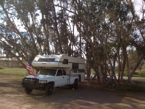1968 Ford Mustang - A truck camper is parked under trees with an American flag flying from the hood.