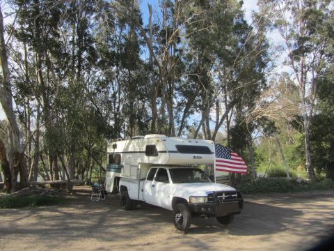 1968 Ford Mustang - A white pickup truck equipped with a camper shell is parked in an outdoor setting, with an American flag displayed nearby.