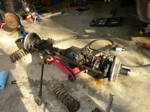 1995 Ford Bronco - The front axle assembly, springs, and other suspension parts are laid out on the garage floor for maintenance.