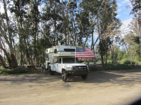 1968 Ford Mustang - A white pickup truck equipped with a camper and flying an American flag is parked in a wooded area.