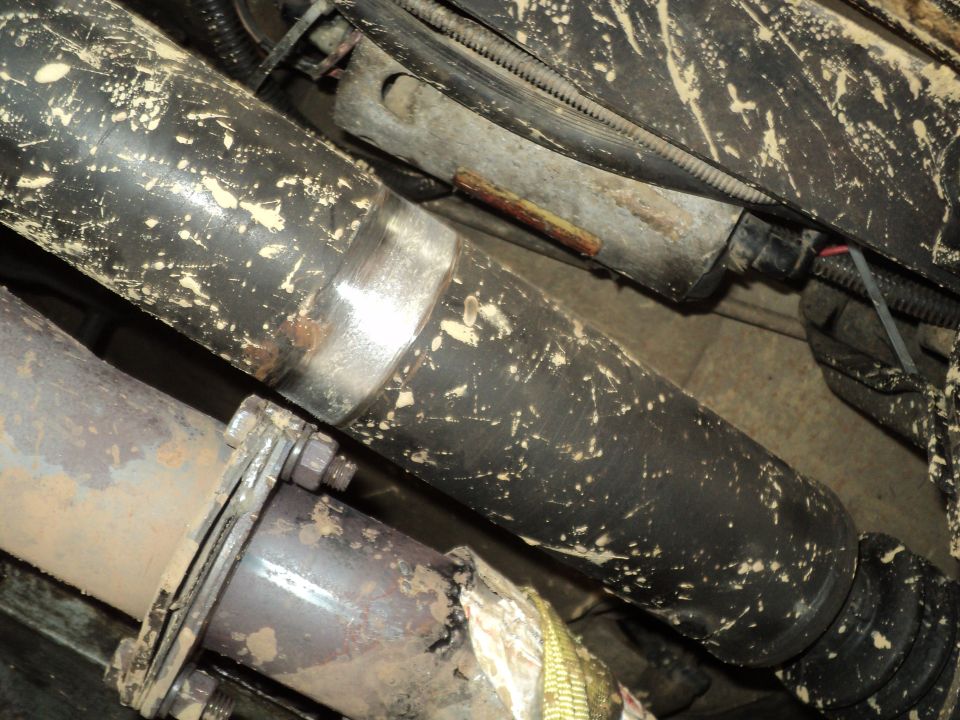 close-up of driveshaft and exhaust pipes, covered in mud splatters. A Supermotors.net watermark is visible