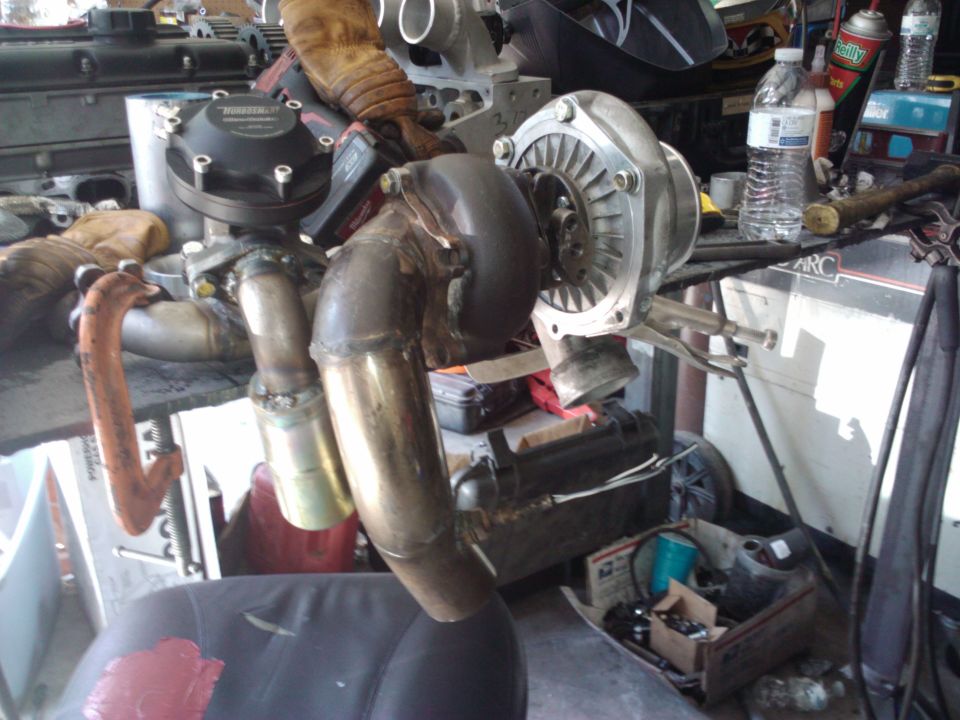 Turbocharger and exhaust manifold assembly on a workbench, with various tools and parts in the background