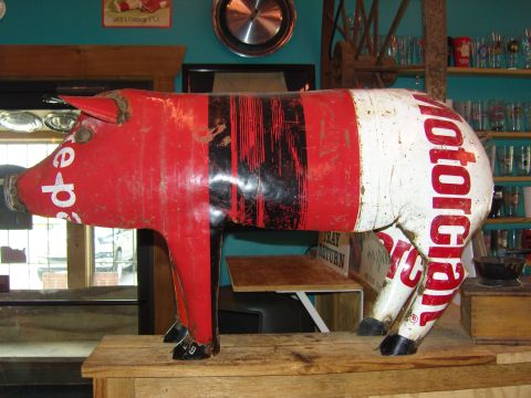 2007 Ford Mustang - A metal pig sculpture with vintage brand text sits on a wooden surface in front of a shelf of glasses.
