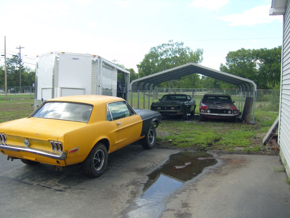 Yellow and black 1967 Ford Mustang coupe, rear view, parked on asphalt with puddles