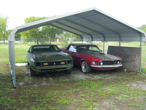 2007 Ford Mustang - A red 1969 Ford Mustang and a green Mustang are parked side-by-side under a metal carport.