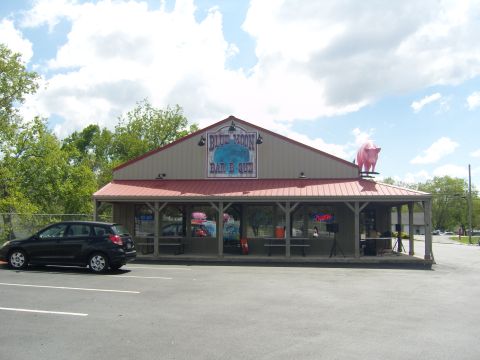 2007 Ford Mustang - A black hatchback is parked in the lot of the Blue Moon Bar & Que, which features a large pink pig statue on its roof.