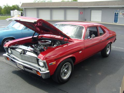 2007 Ford Mustang - A red classic coupe is parked with its hood open, revealing the engine bay. Another vehicle is visible to the left.