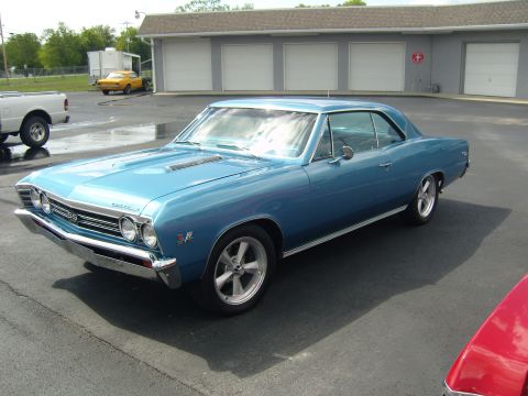 2007 Ford Mustang - A blue 1967 Chevrolet Chevelle SS coupe is parked outside a building with garage doors.