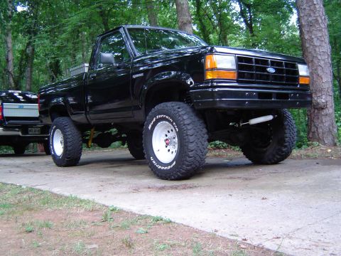 1989 Ford Ranger - A lifted black 1989 Ford Ranger pickup truck is shown from a 3/4 front angle, with another truck visible in the background.