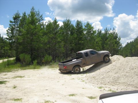 1994 Ford Bronco - A gray pickup truck navigates an off-road course, climbing a large pile of light-colored gravel.