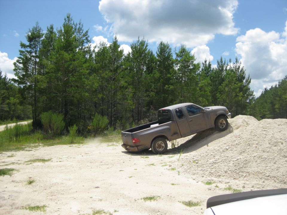 Gray pickup truck driving up a dirt pile, side view