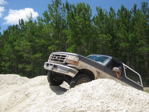 1994 Ford Bronco - Ford Bronco navigates sandy terrain under a blue sky with scattered clouds.