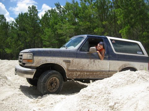 1994 Ford Bronco - A person smiles from the window of a muddy Ford Bronco partially buried in a sand dune.