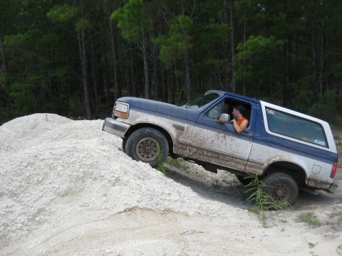 1994 Ford Bronco - A blue and white Ford Bronco navigates a sandy incline with a driver inside.