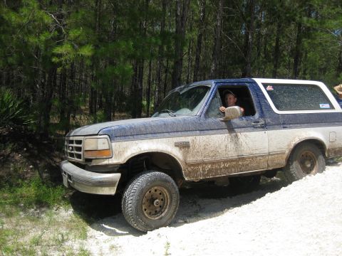 1994 Ford Bronco - Mud-covered 1994 Ford Bronco navigates a wooded trail.