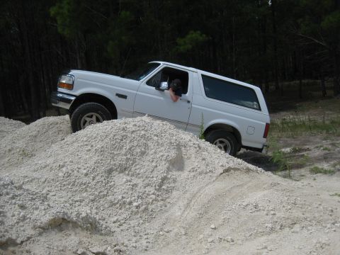 1994 Ford Bronco - A white 1994 Ford Bronco navigates a sandy incline in a wooded area.