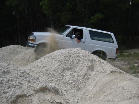 1994 Ford Bronco - A white Ford Bronco navigates a sandy terrain, with dust billowing around it.