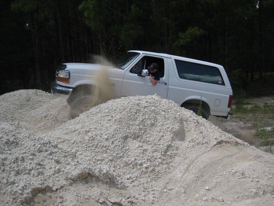White Ford Bronco driving through a sand pile, kicking up dust