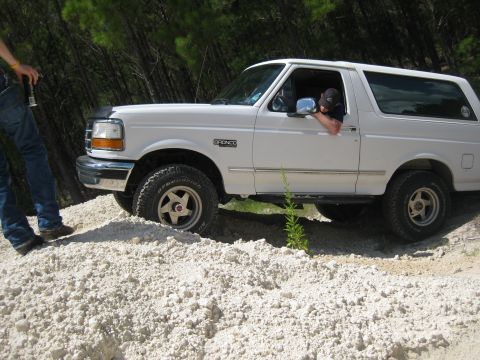 1994 Ford Bronco - White 1994 Ford Bronco navigates a sandy incline, with a person visible in the driver's seat.