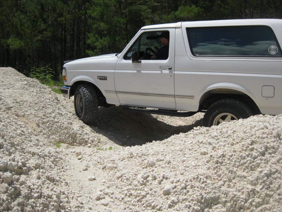 White 1994 Ford Bronco driving over a pile of light-colored dirt