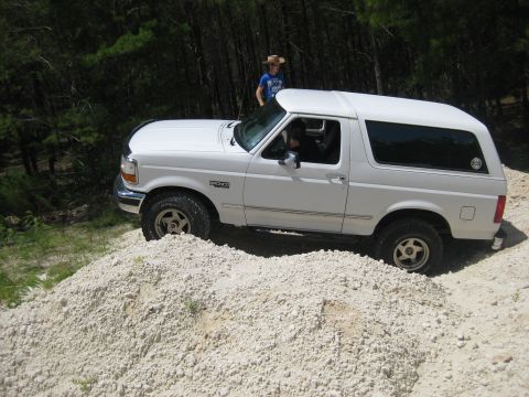 1994 Ford Bronco - A white 1994 Ford Bronco is shown from a 3/4 front angle, parked on a pile of dirt with trees in the background.