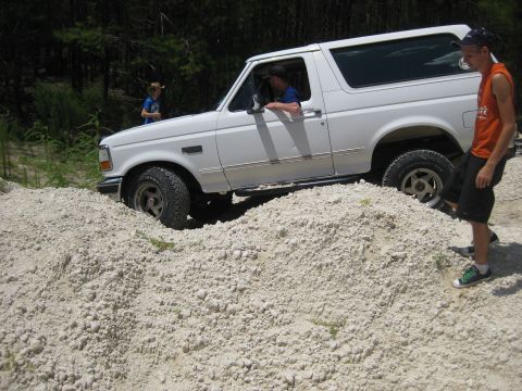 1994 Ford Bronco - A white Ford Bronco navigates a rocky terrain, with two onlookers observing the off-road adventure.