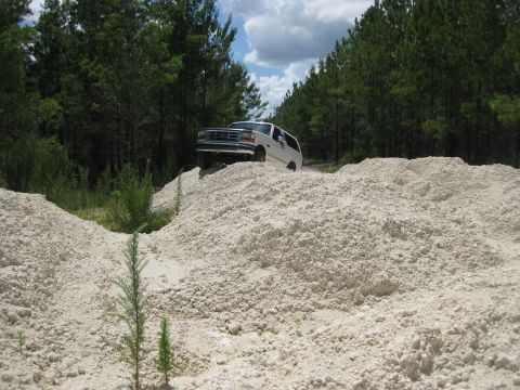 1994 Ford Bronco - White 1994 Ford Bronco navigates a sandy hill in a wooded area.