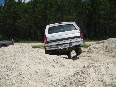 1994 Ford Bronco - A white Ford Bronco navigates a sandy off-road course, with another vehicle visible in the background.