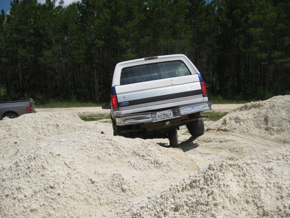 White Ford Bronco with blue stripe, rear view, driving off-road over sand mounds
