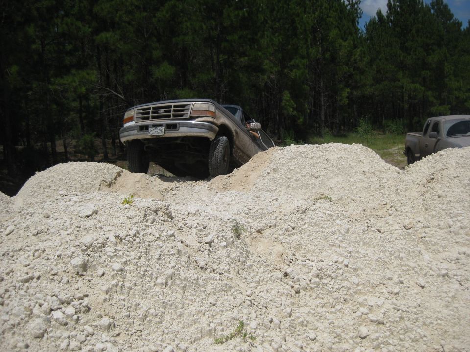 1994 Ford Bronco climbing over dirt mounds with another truck in the background