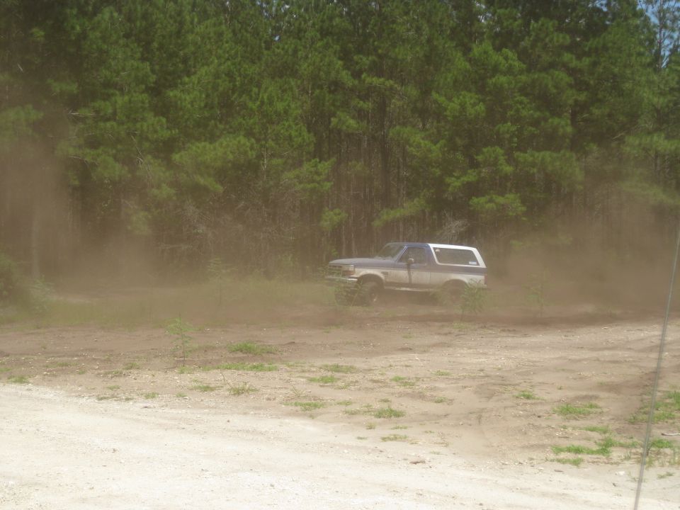 1994 Ford Bronco kicking up dust while driving on a dirt road near trees