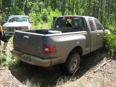 1994 Ford Bronco - A muddy Ford F-150 is parked off-road, with another truck visible in the background.