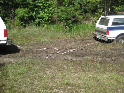 1994 Ford Bronco - Two SUVs are stuck in the mud, connected by a tow strap, with trees and grass in the background.