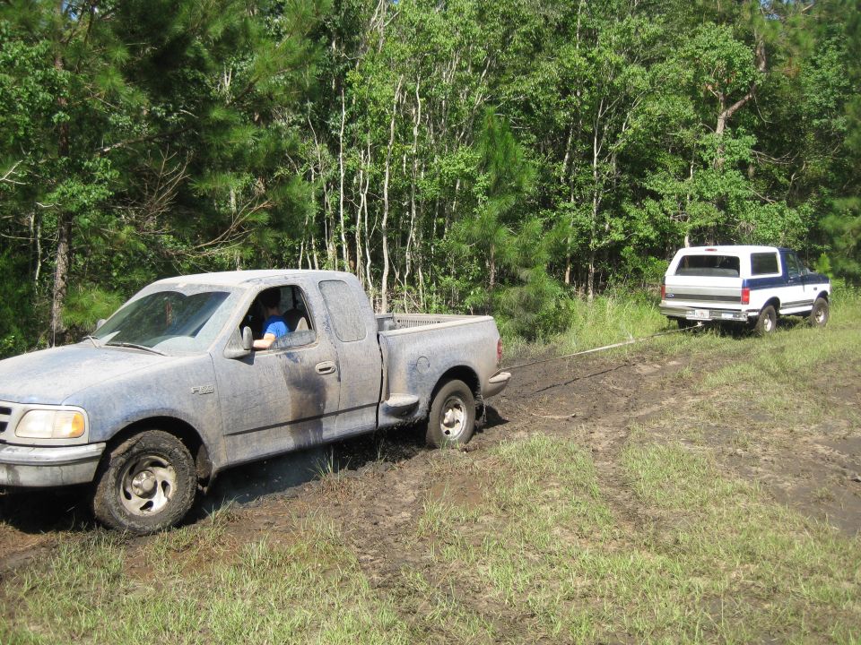 Muddy blue Ford F-150 towing a white and blue Ford Bronco off-road